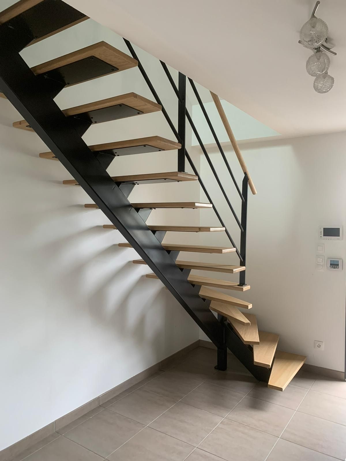 Escalier moderne et flottant avec marches en bois clair, structure et rampe en métal noir, murs blancs.