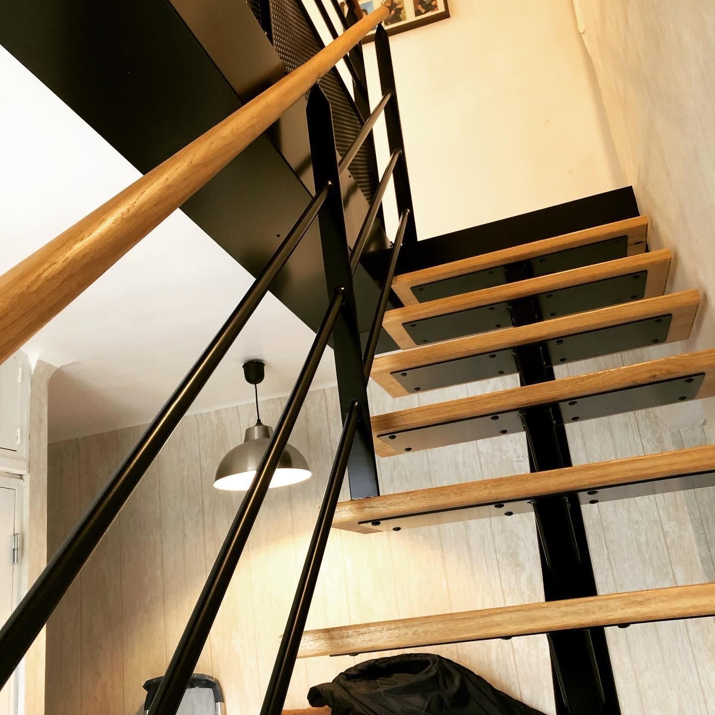 Escalier en bois avec supports en métal noir et rampe en bois. Intérieur moderne et industriel.