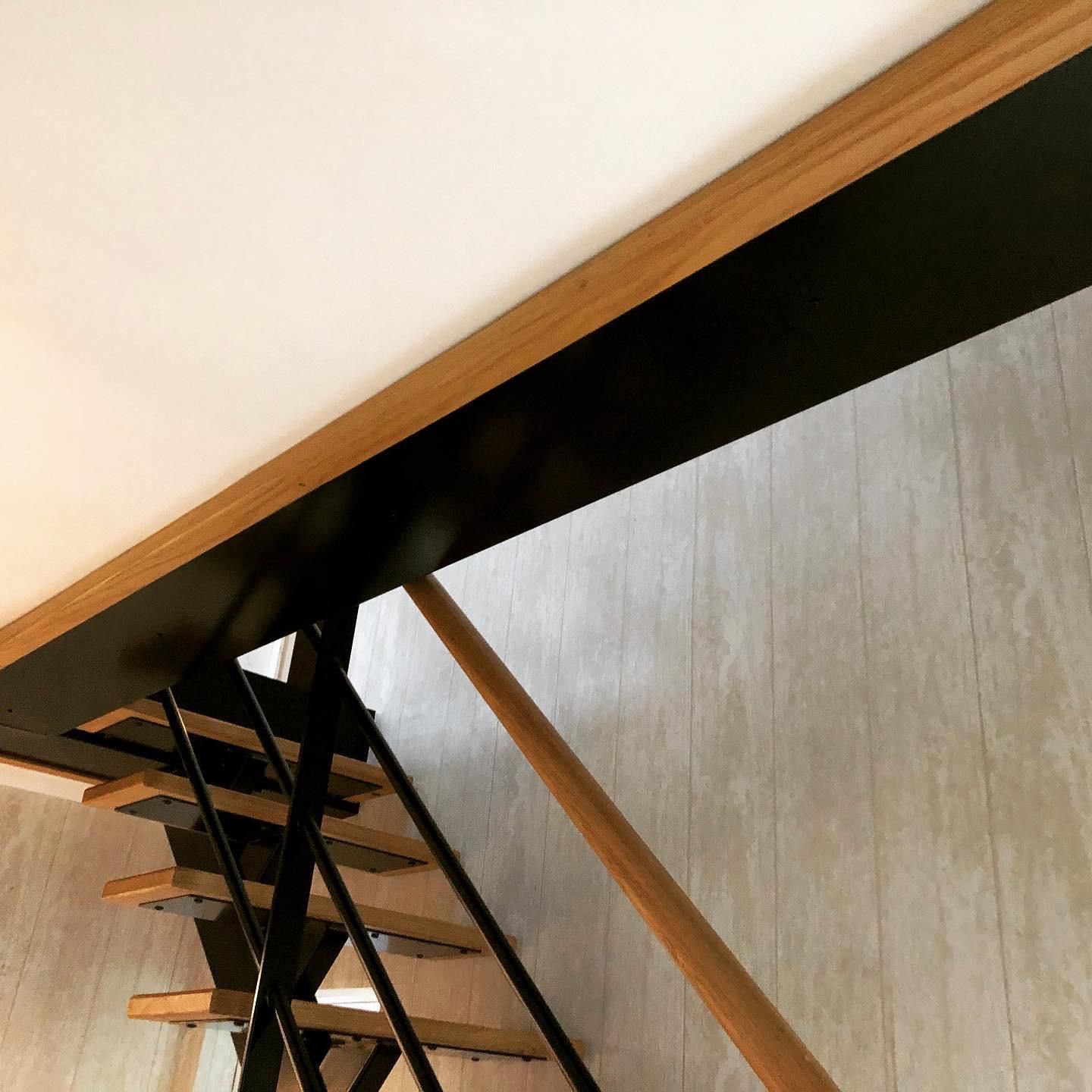 Escalier en métal noir avec marches et rampe en bois contre un mur gris clair.