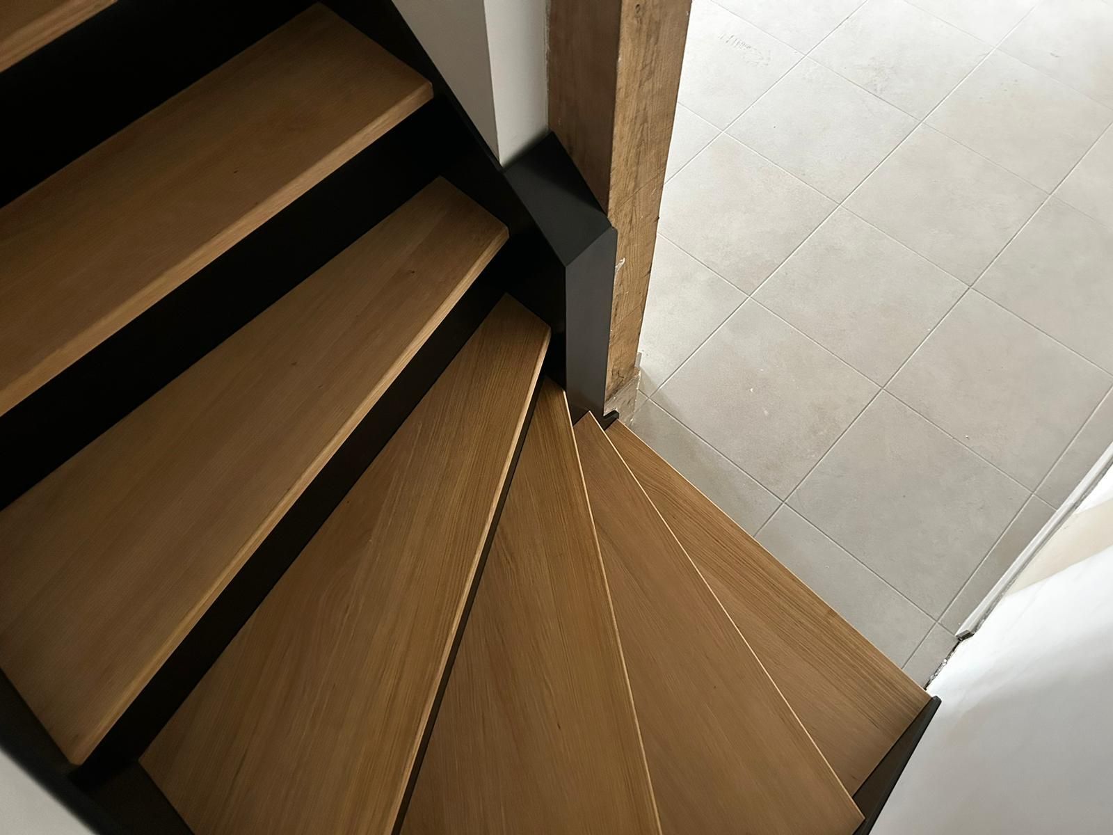 Escalier en colimaçon en bois avec garniture noire, menant vers le haut à côté d'un sol carrelé.