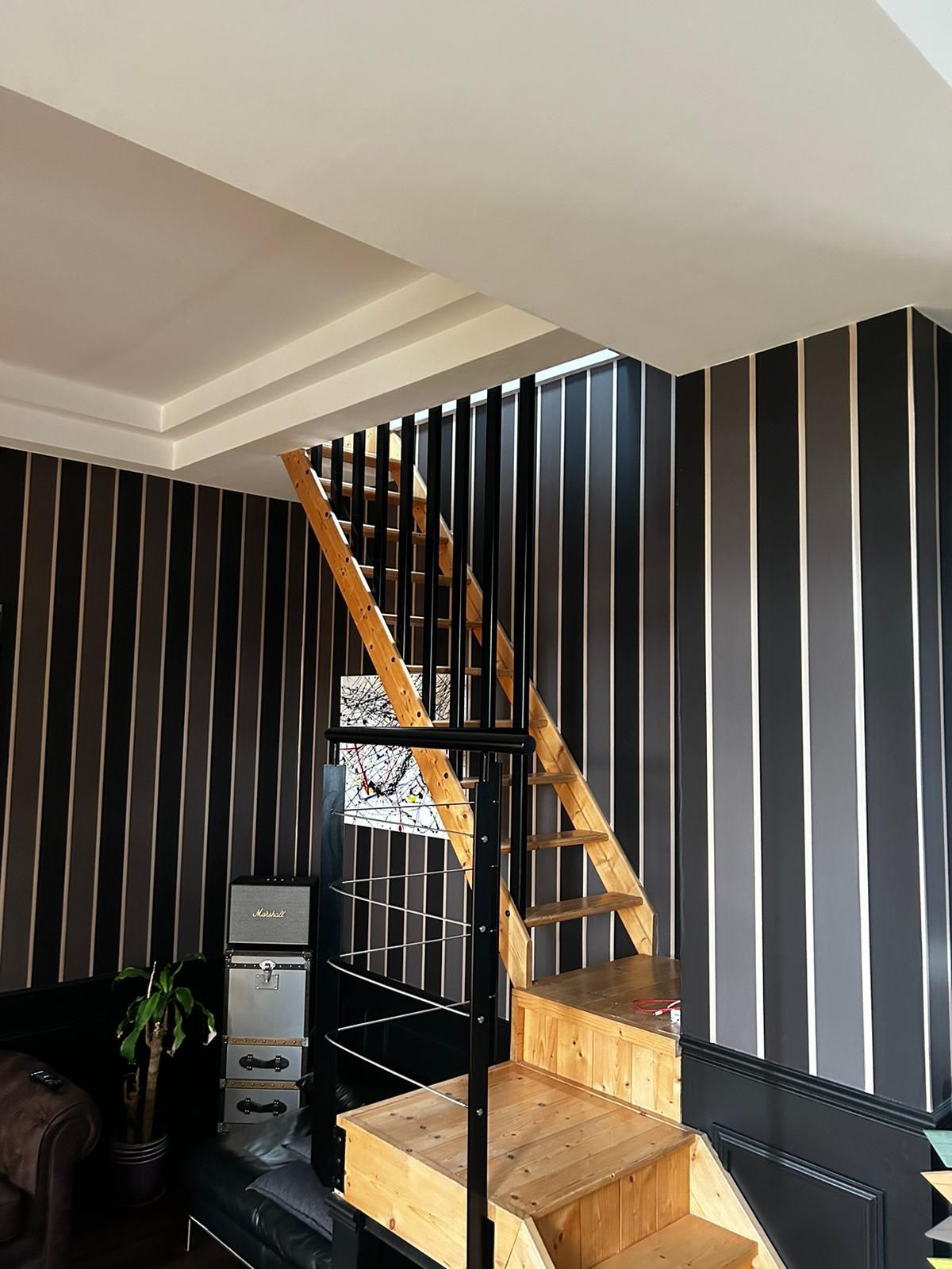 Vue intérieure d'un escalier en colimaçon avec marches en bois et rampes noires, sur fond de papier peint à rayures.