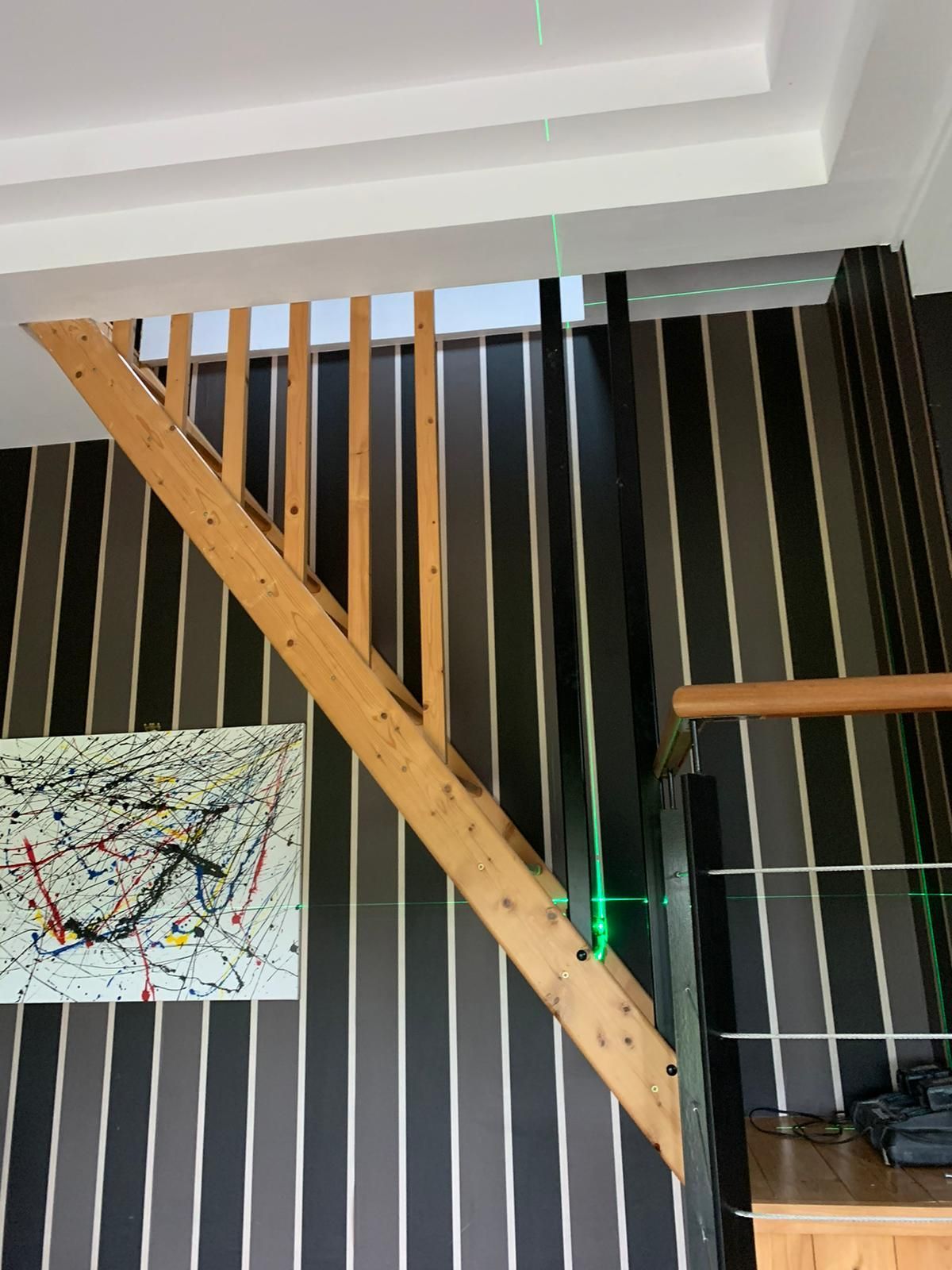 Escalier en bois avec rampe verticale contre un mur rayé. Niveau laser vert indiquant le niveau.