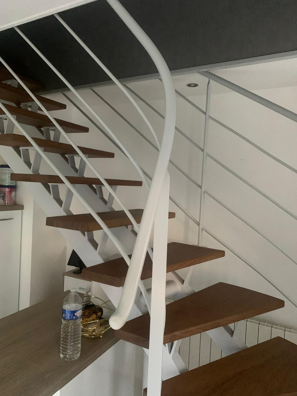Escalier en bois avec rampe en métal blanc, bouteille d'eau et petits objets décoratifs.