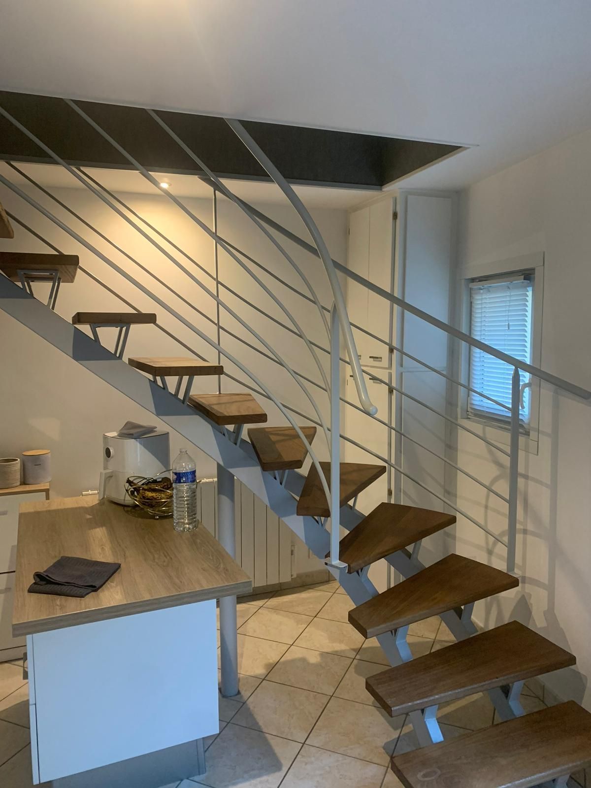 Escalier moderne avec marches en bois, rampes en métal et une petite fenêtre.