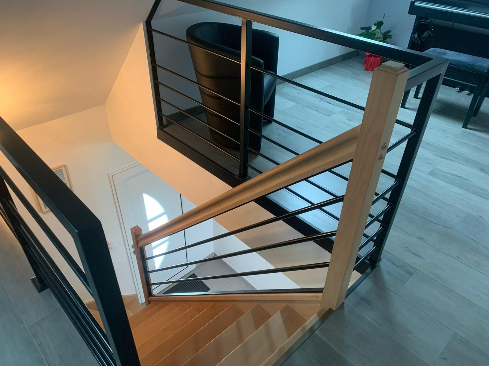 Escalier avec marches en bois et rampe en métal noir. Intérieur de maison moderne avec une chaise sombre visible.