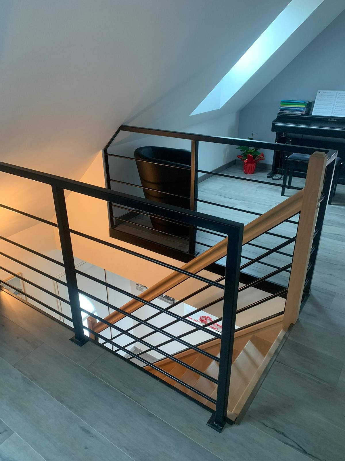 Vue intérieure d'une cage d'escalier avec rampe en métal noir et main courante en bois dans un cadre mansardé.