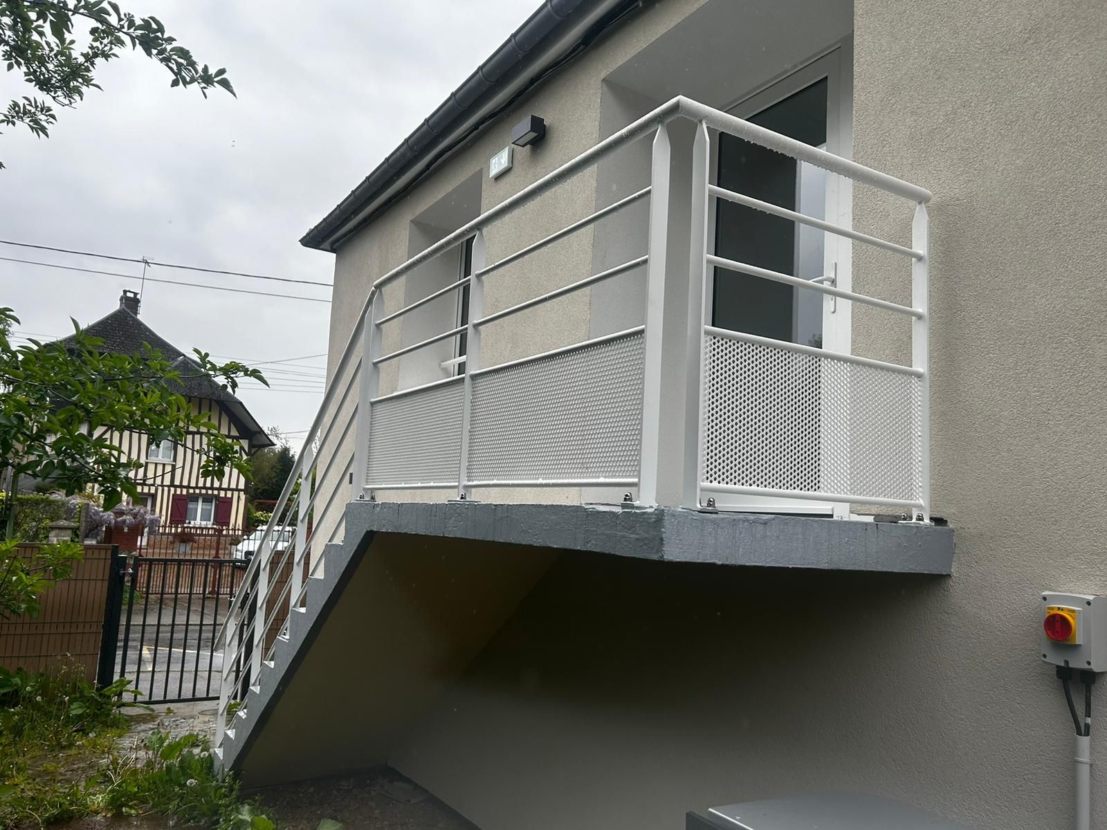 Vue extérieure d'un escalier en béton gris avec rampe blanche menant à un balcon.