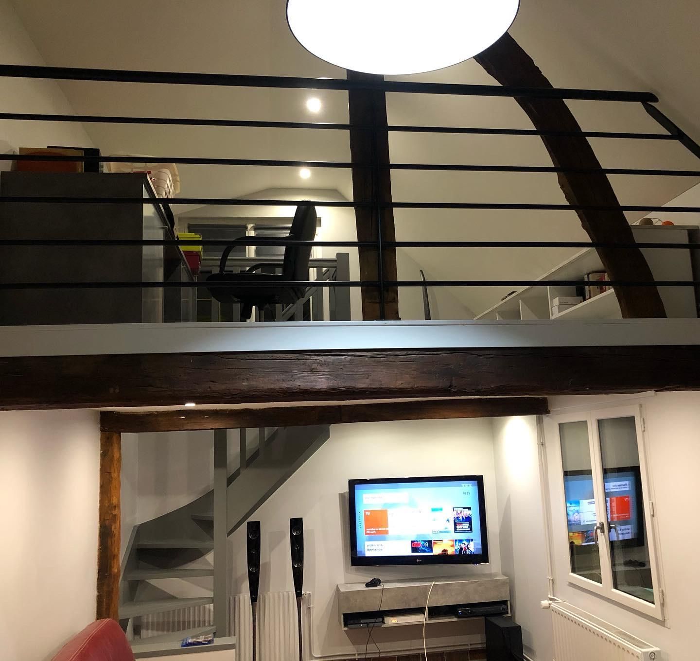 Intérieur d'un appartement loft avec une télévision, un escalier et un niveau supérieur avec un bureau et une chaise.