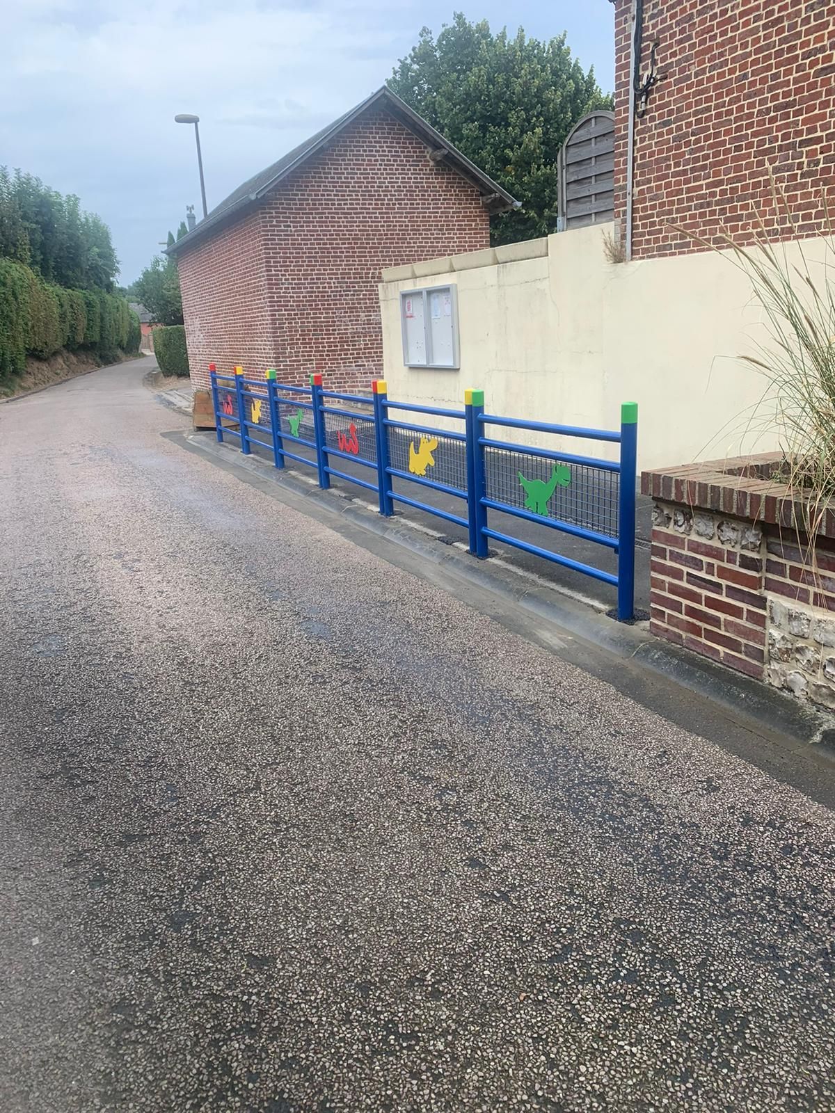 Clôture bleue avec des décorations colorées le long d'une rue devant des bâtiments en briques et de couleur crème.