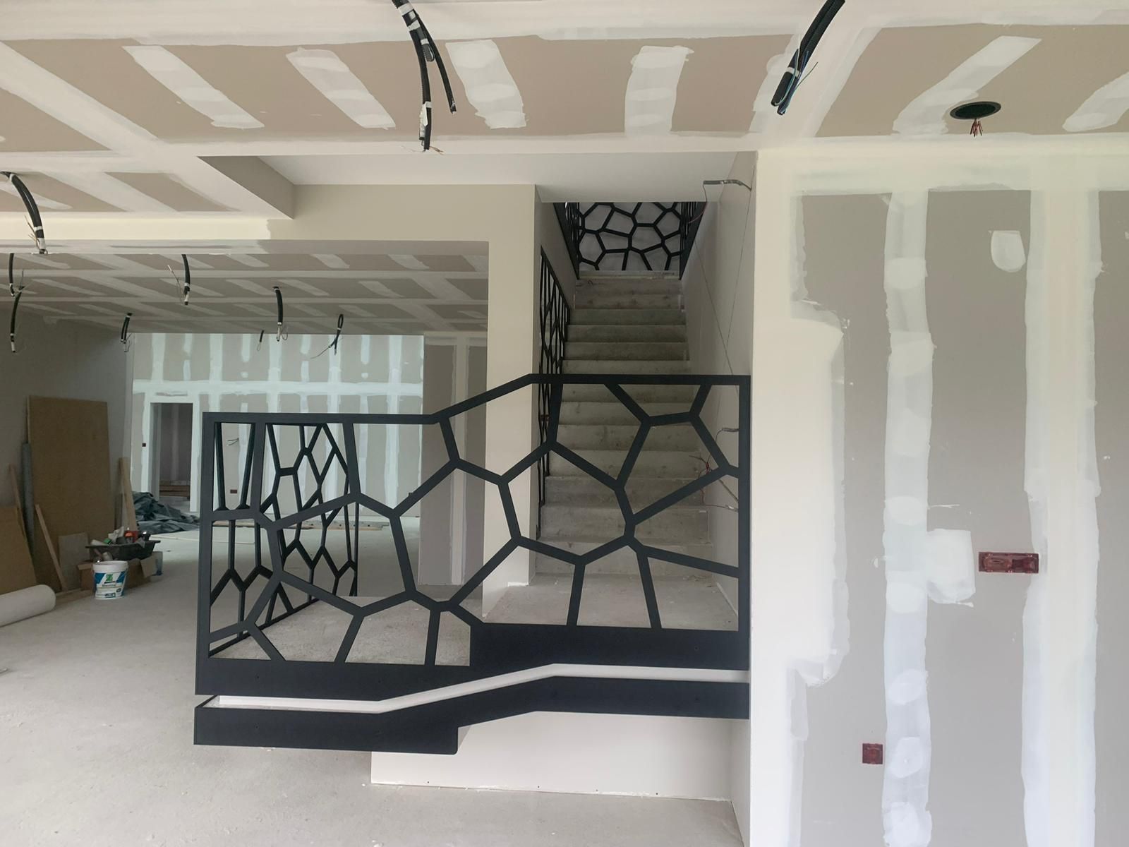 Vue intérieure d'un escalier avec rampe géométrique noire, en construction. Cloisons sèches, câblage apparent et plafond brut.