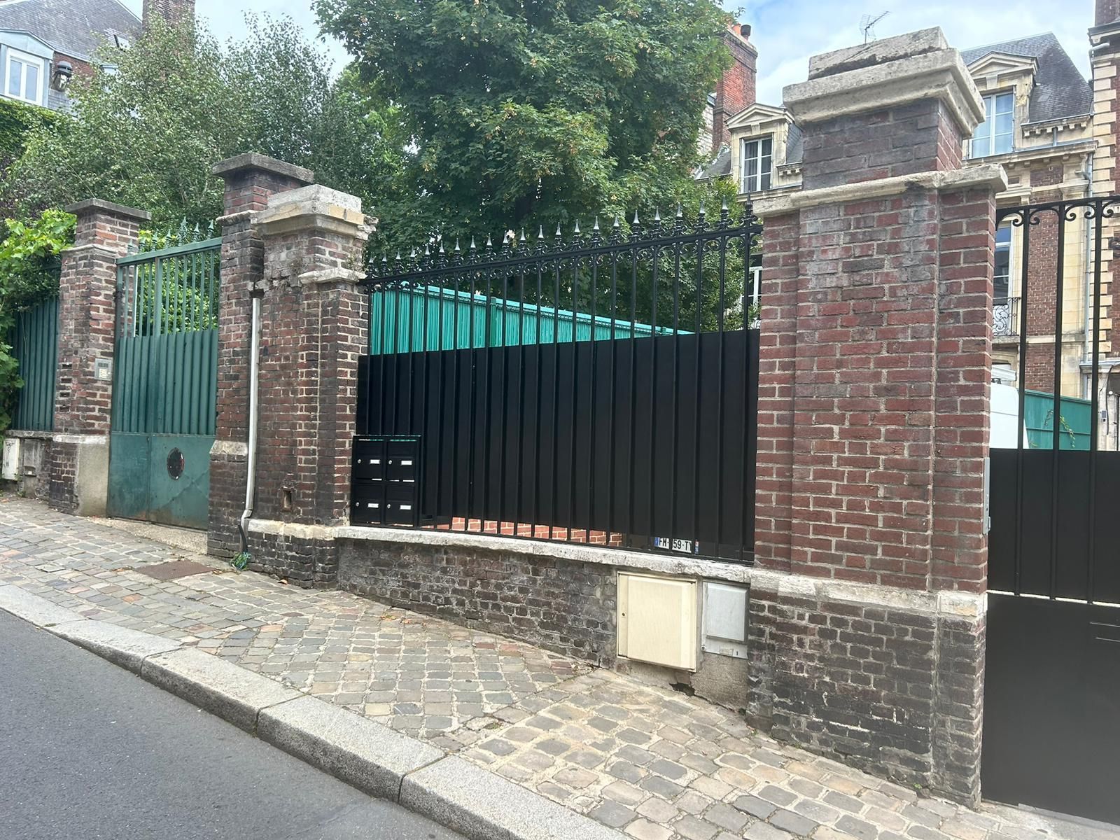 Clôture en brique et fer forgé avec portail sur une rue pavée.