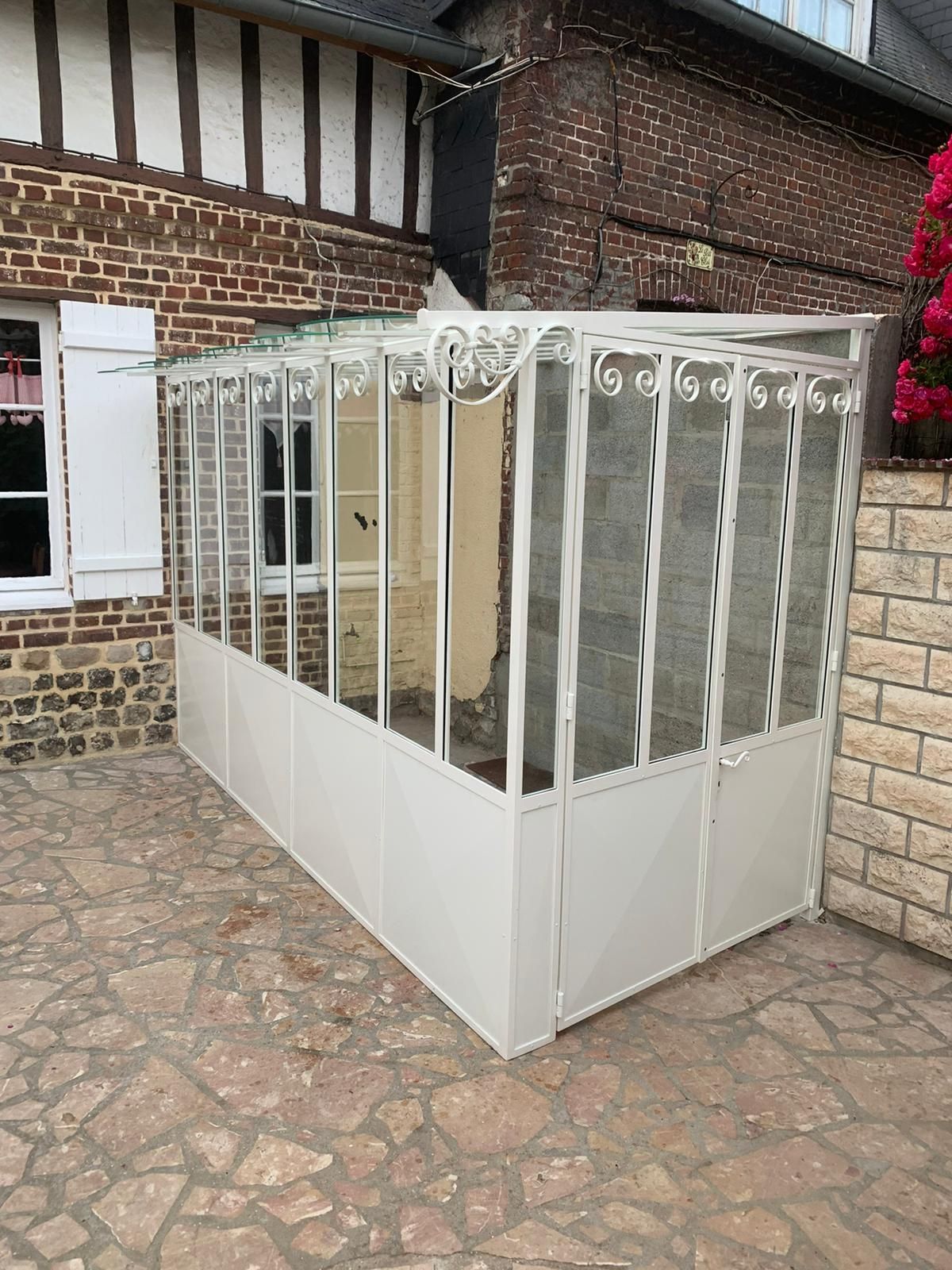 Véranda en verre blanc et métal contre un bâtiment en briques avec patio en pierre.