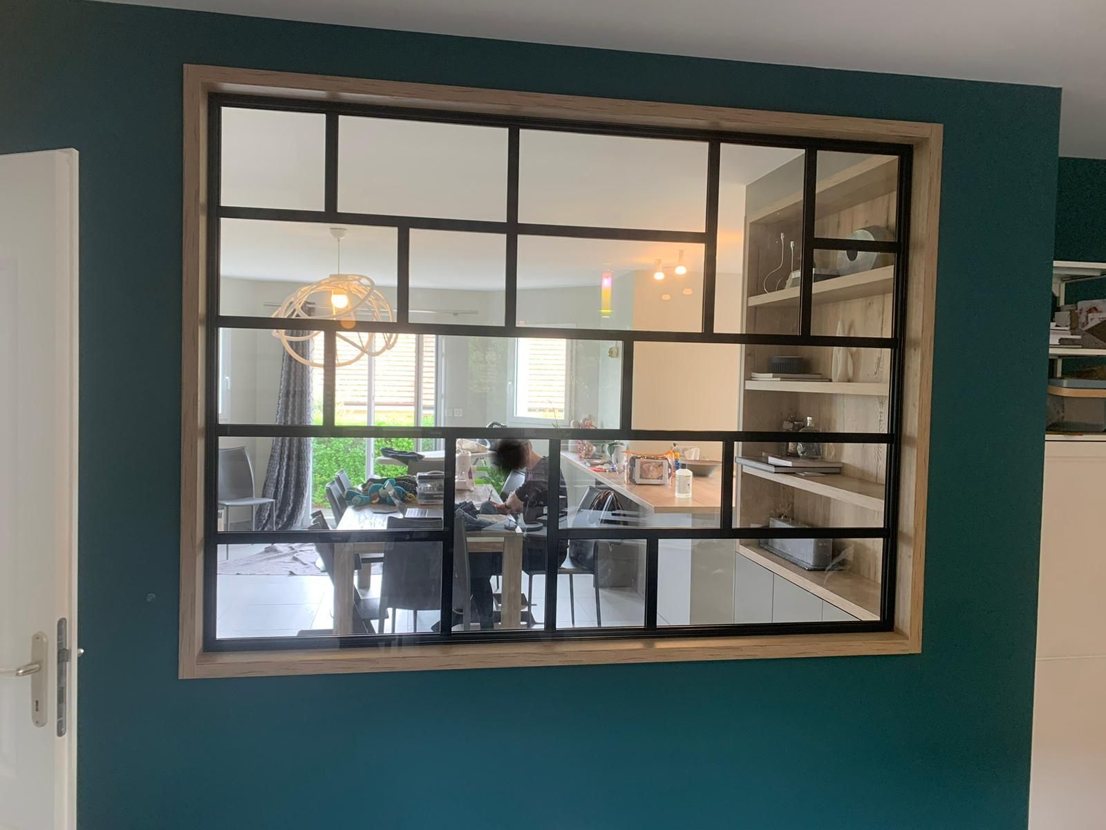 Fenêtre à cadre noir avec plusieurs vitres, montrant une salle à manger avec un mur bleu sarcelle foncé.
