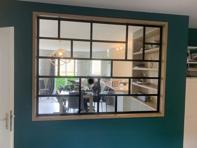 Fenêtre à cadre noir avec plusieurs vitres, montrant une salle à manger avec un mur bleu sarcelle foncé.
