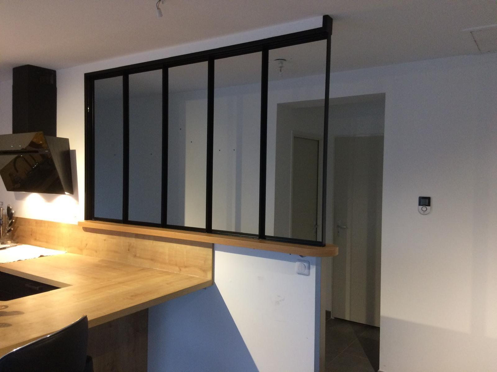 Cloison en verre à cadre noir séparant la cuisine du couloir, sur un comptoir en bois.