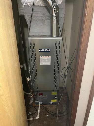 A furnace is sitting in a corner of a room next to a door.