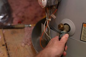 A person is fixing a water heater with a screwdriver.