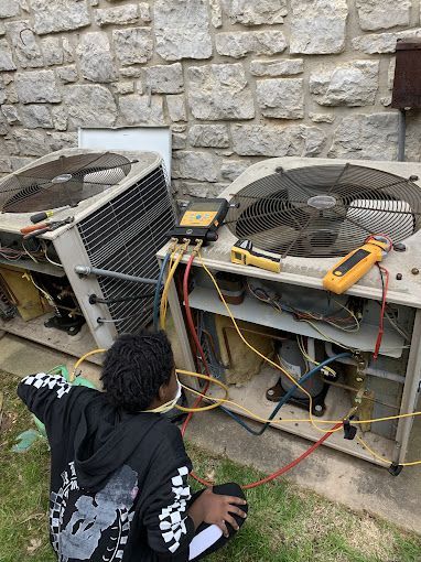 A man is kneeling down in front of an air conditioner.