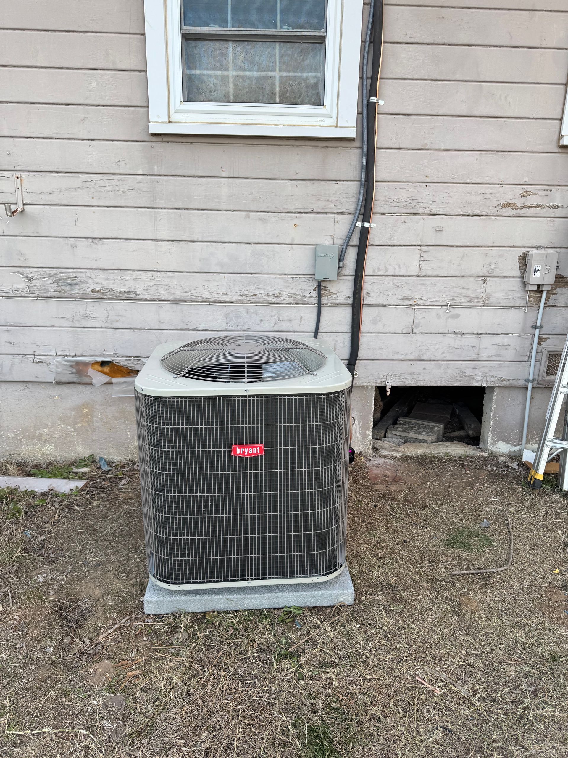 An air conditioner is sitting outside of a house next to a window.
