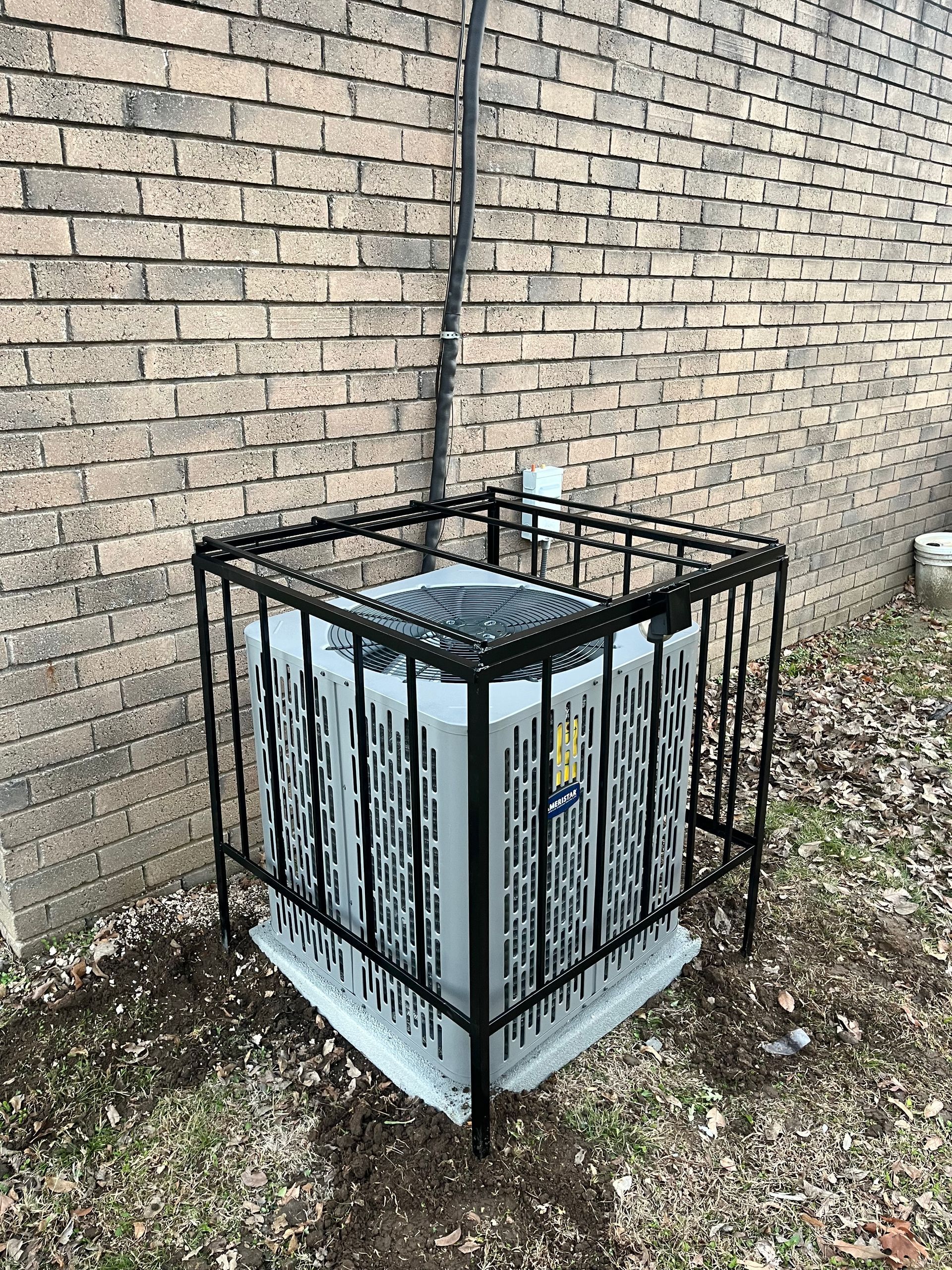 An air conditioner is sitting in front of a brick wall in a cage.