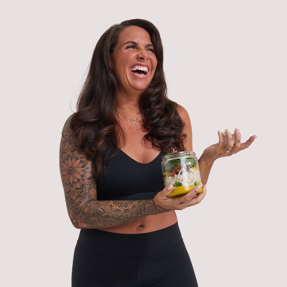 A woman is holding a jar of food and laughing.  - Average Jenn's - Personalized Workout and Nutrition Plans