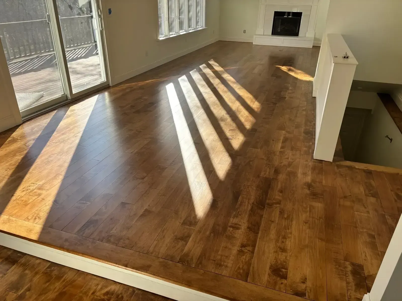 Sunlit empty room with wood flooring, angled skylight shadows, and a stair opening on the right