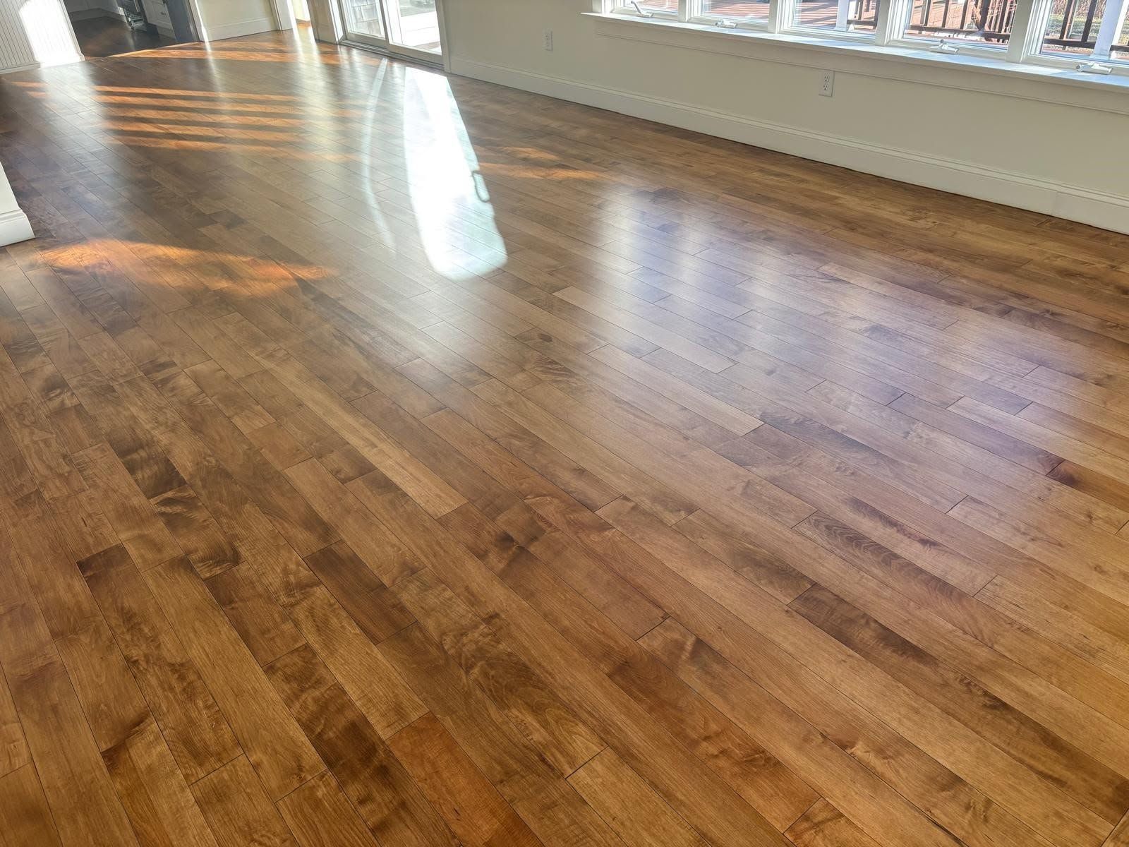 Sunlit hardwood floor in an empty room with windows and white baseboards