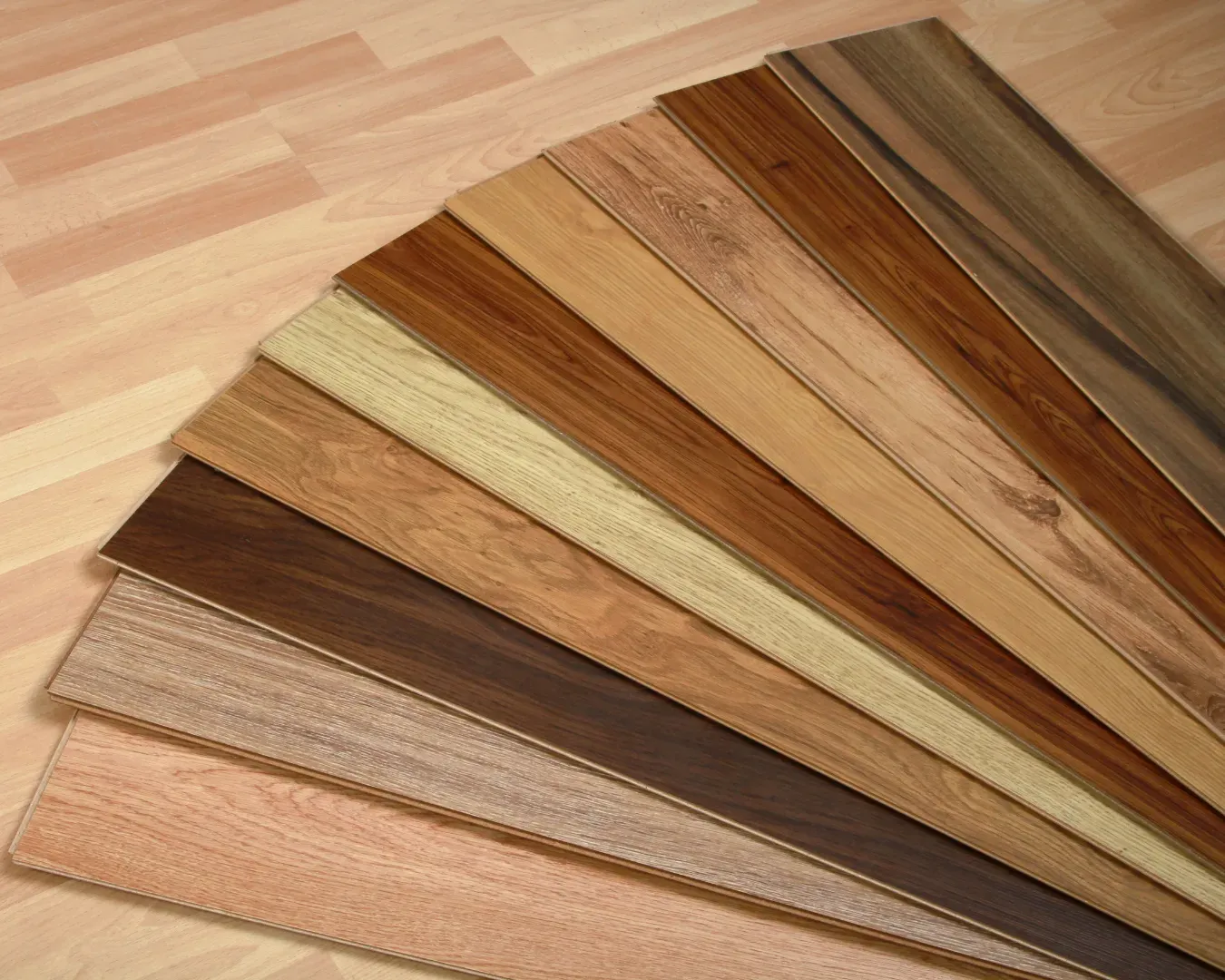 Assorted wood flooring planks fanned out in different shades of brown, tan, and gray on a light wood floor