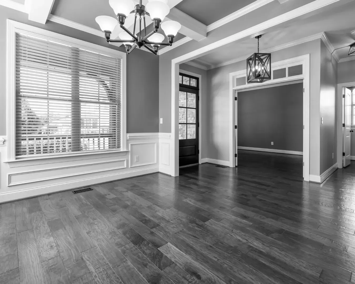Empty dining room with hardwood floors, large window, chandelier, and doorway to adjoining room.