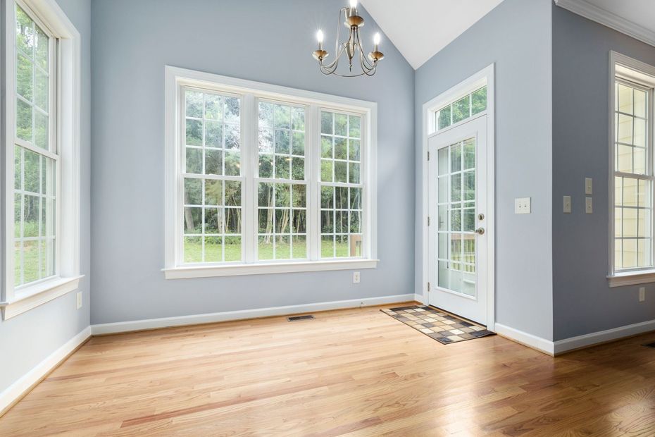 Empty sunlit room with light blue walls, hardwood floors, and large windows.
