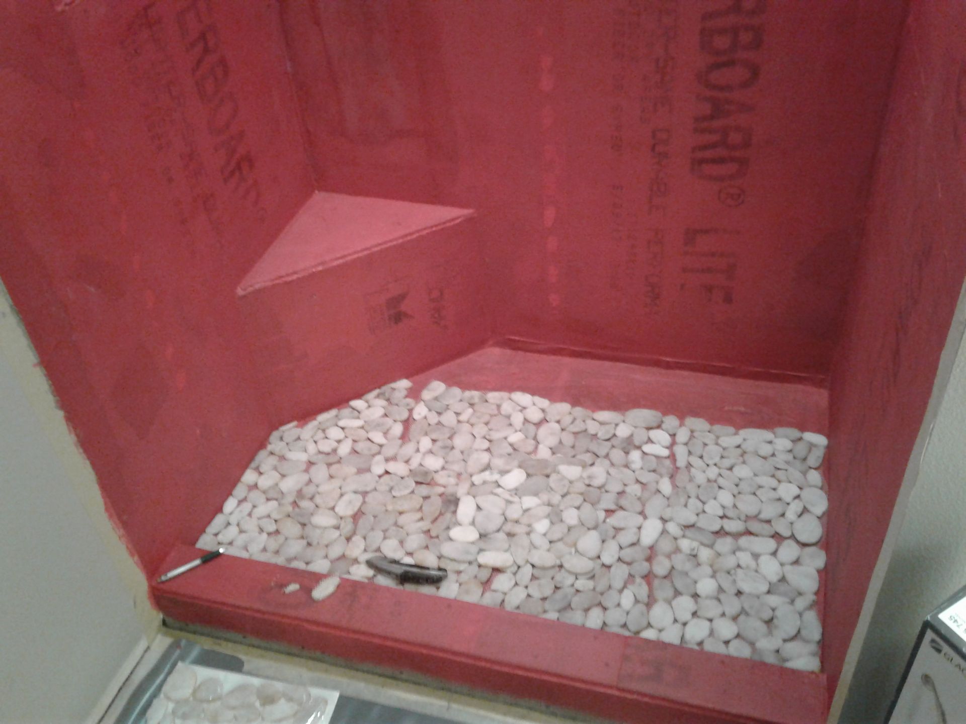 A shower with a red wall and white rocks on the floor.
