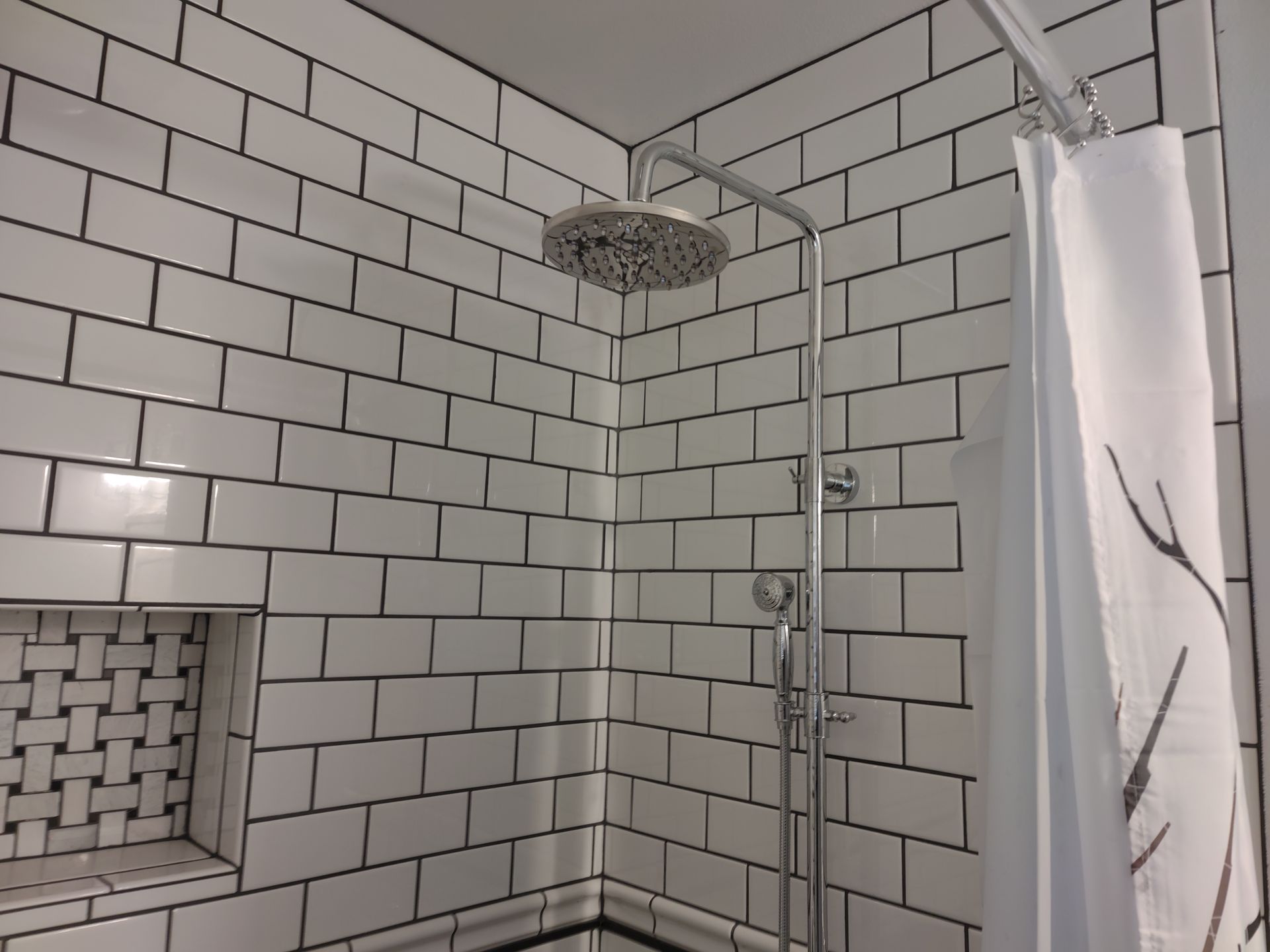 A shower with white tiles and a shower head