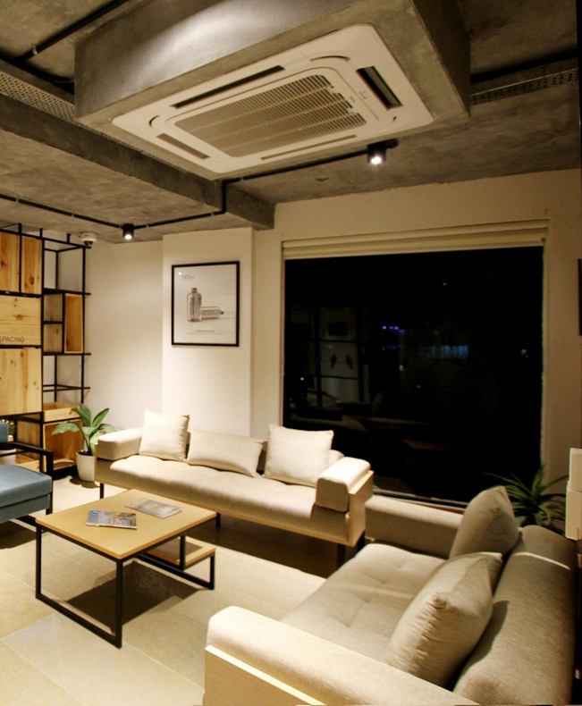Modern living room with beige sofas, a coffee table, and a ceiling air conditioner at night.