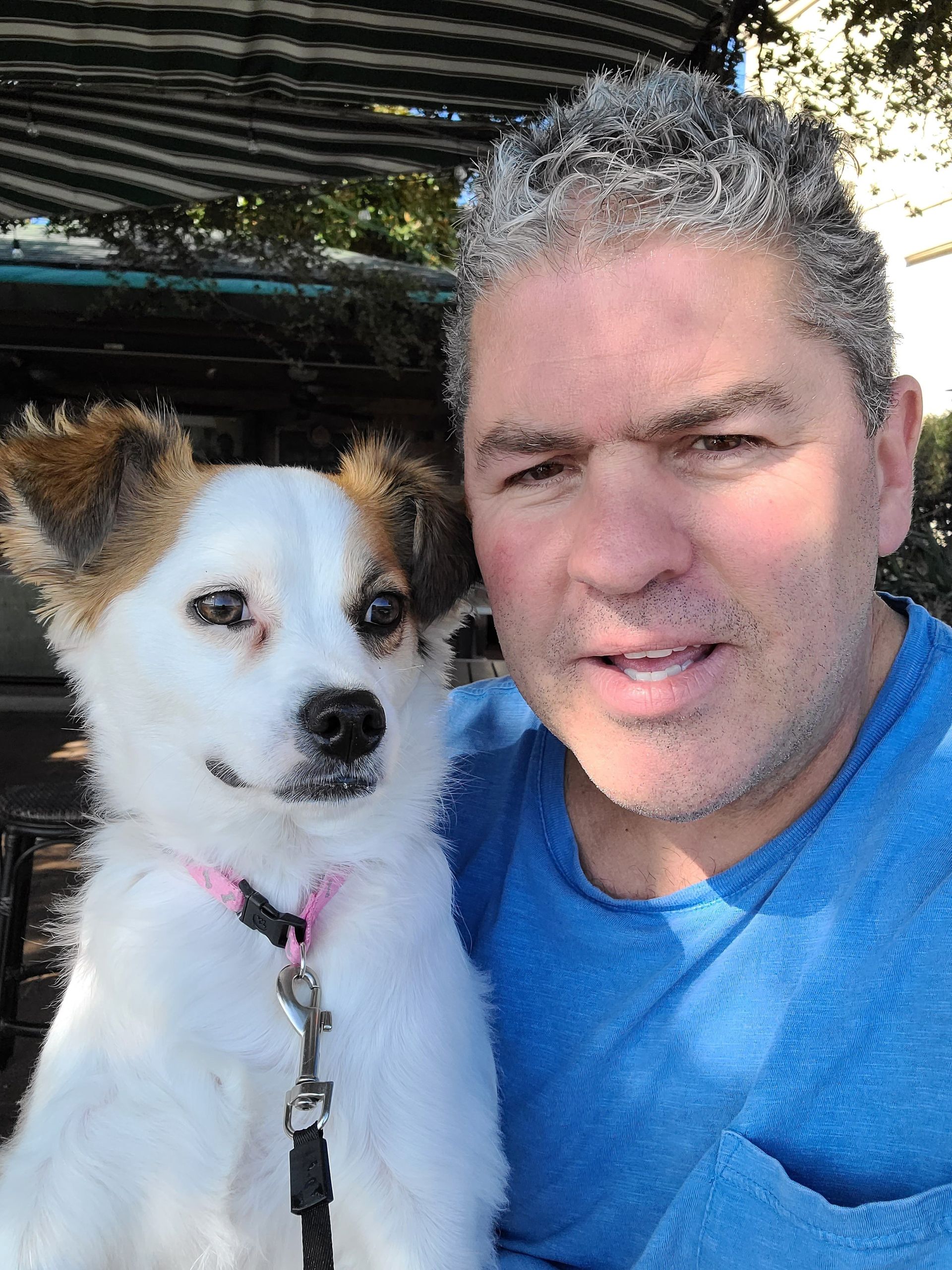Man and small white dog taking a selfie outdoors in sunlight