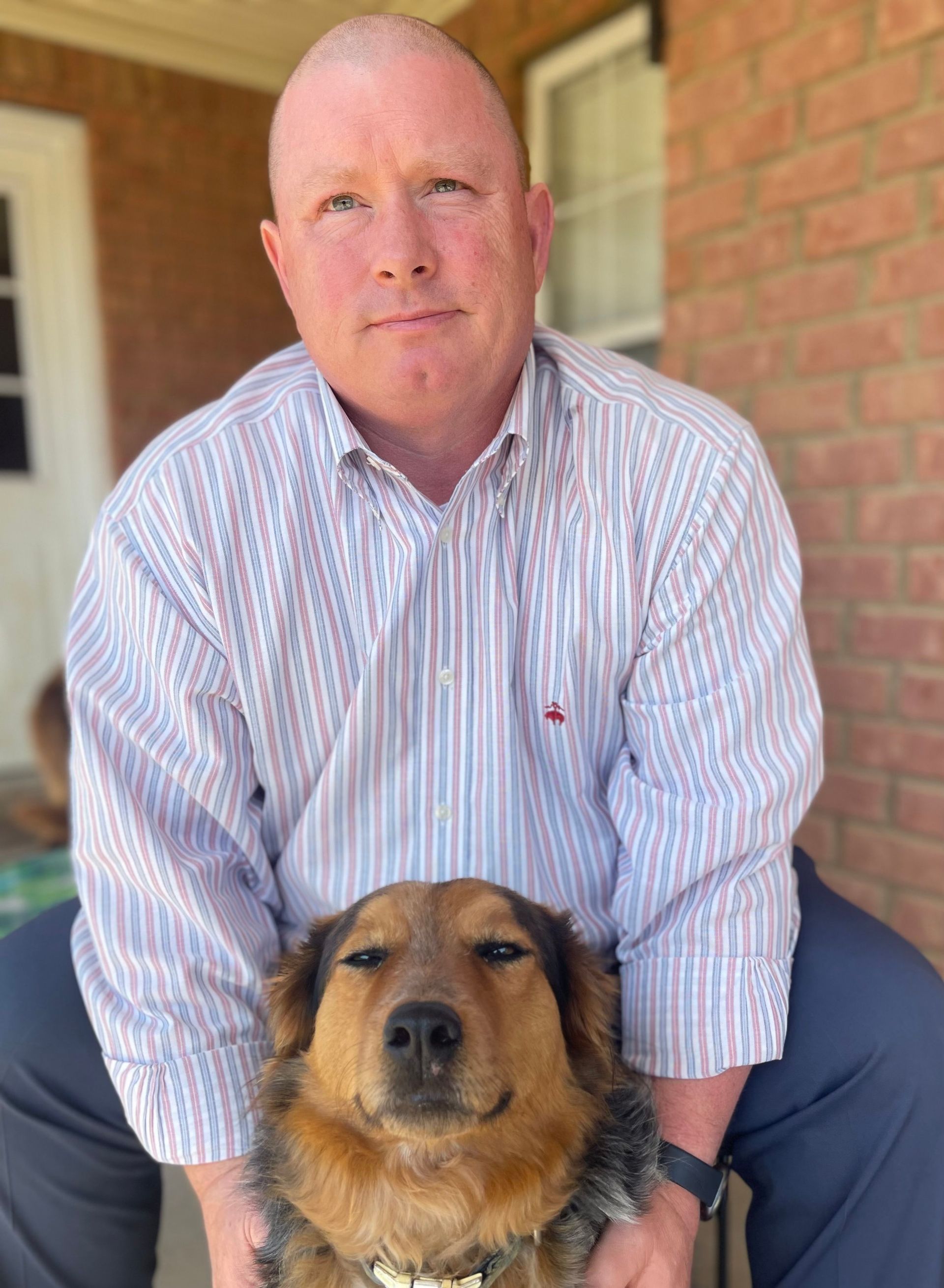Man sitting on a porch with a brown dog in front of him, brick wall and doorway behind them