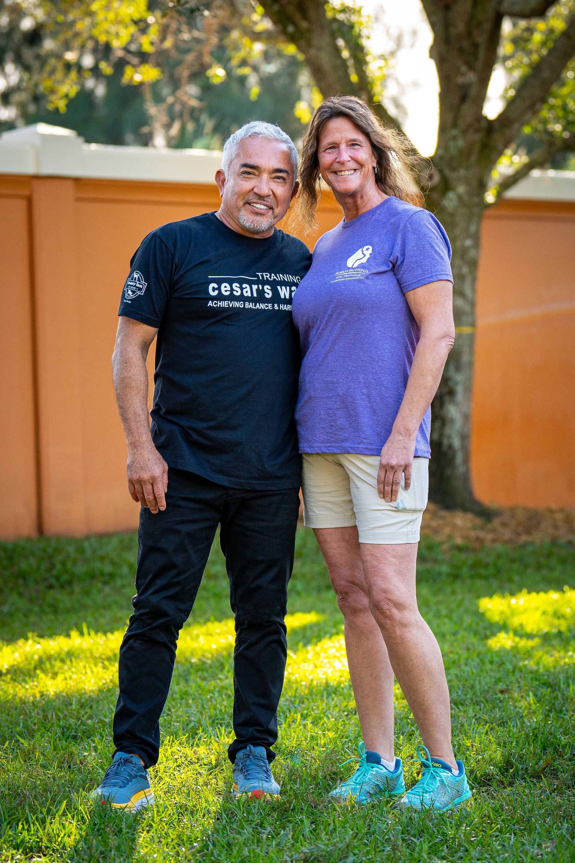Two people standing on grass outdoors, smiling in casual shirts and shorts.