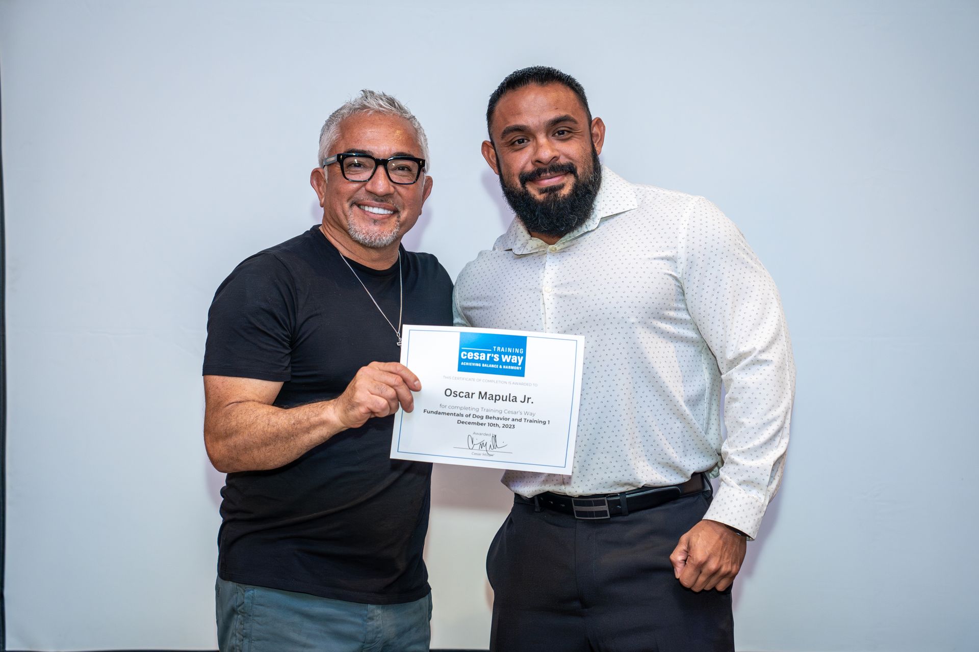 Two men smile while holding a certificate against a plain light background.
