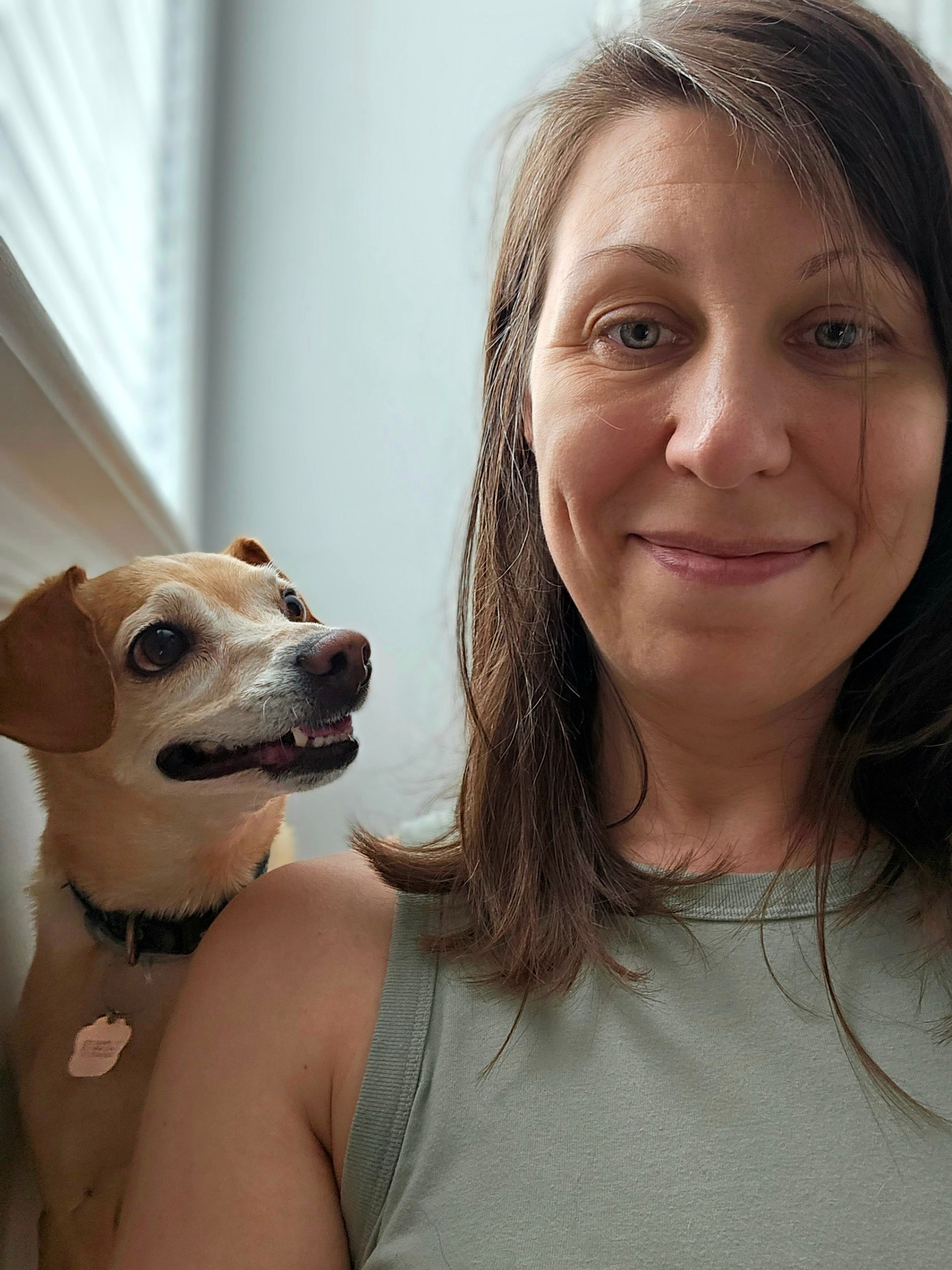 Woman smiling indoors beside a small tan-and-white dog looking up at her