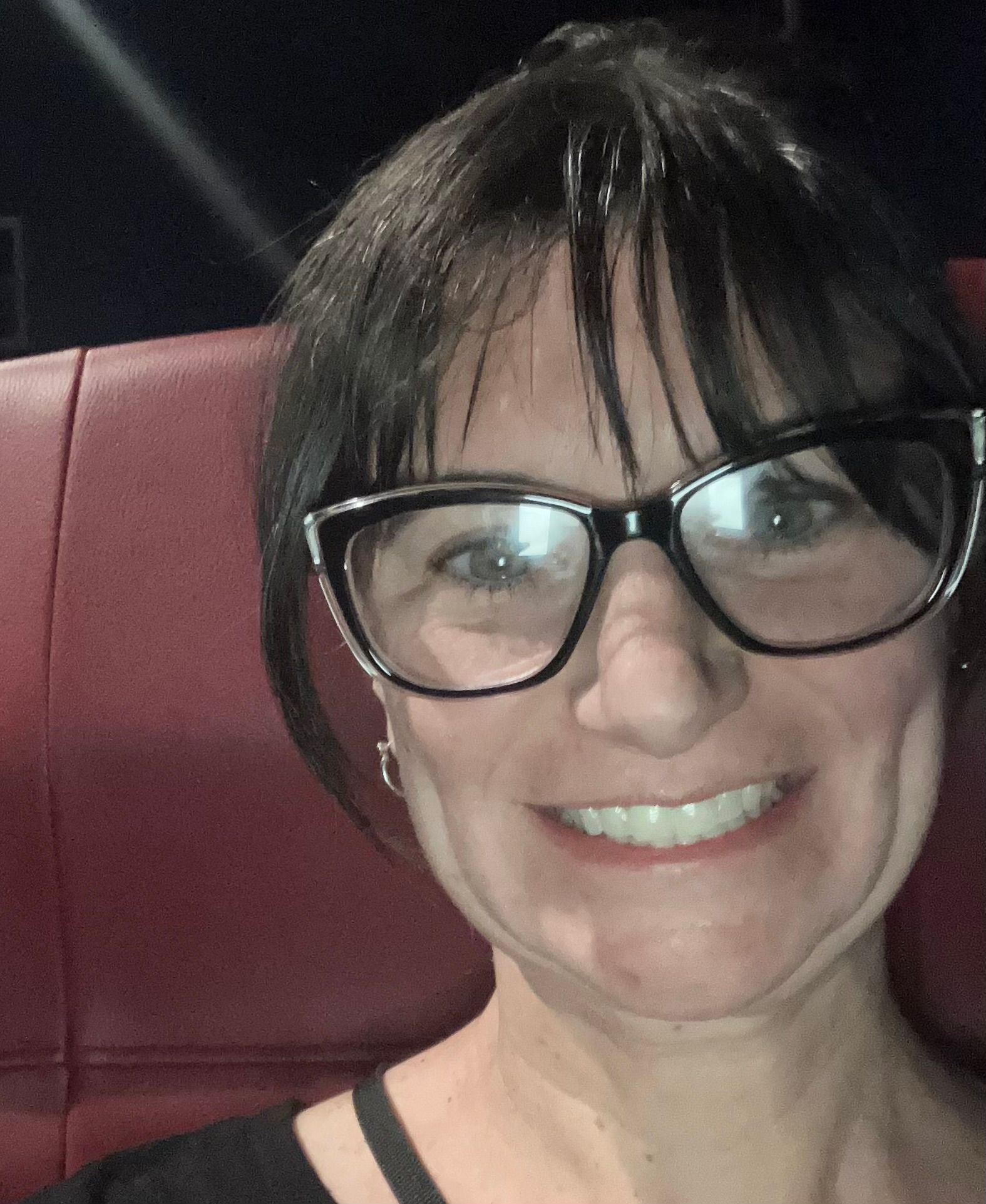 Smiling person with black glasses seated against a red upholstered seat
