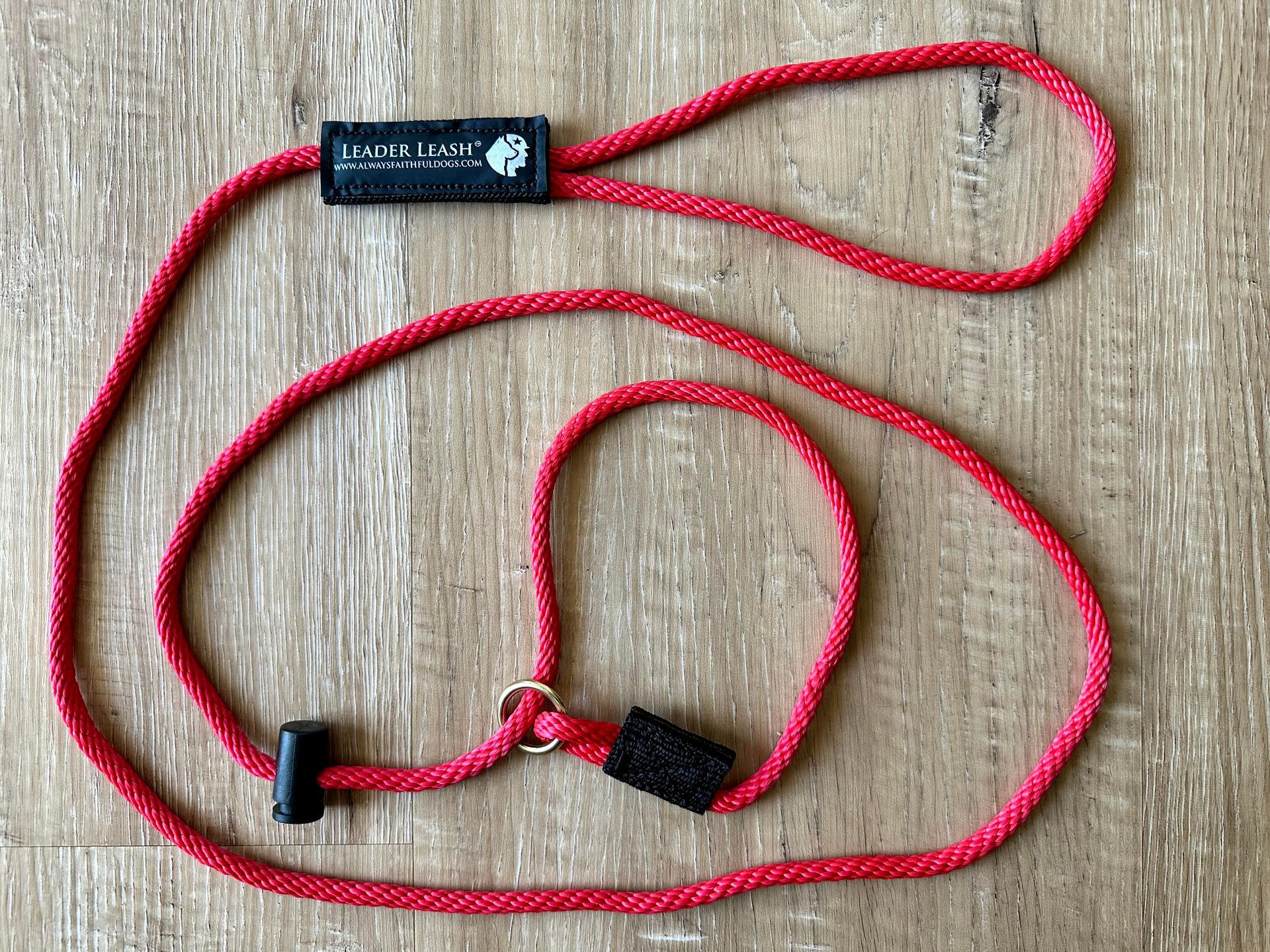 Red lanyard with black clip and cord laid in loops on a wood surface.