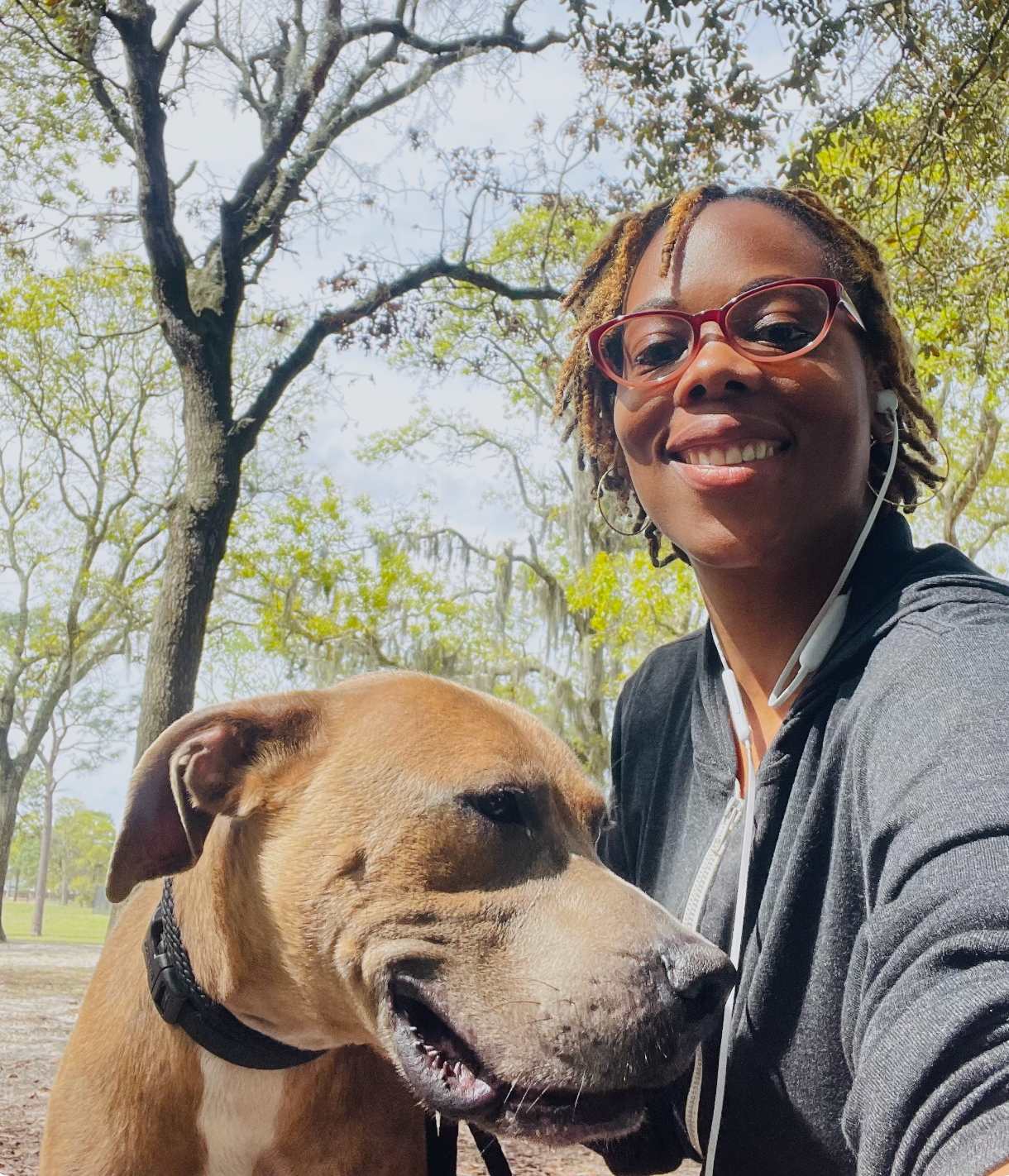 Woman smiling with a tan dog in a sunny park with trees