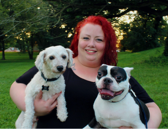 Woman with red hair holding two dogs in a park at sunset