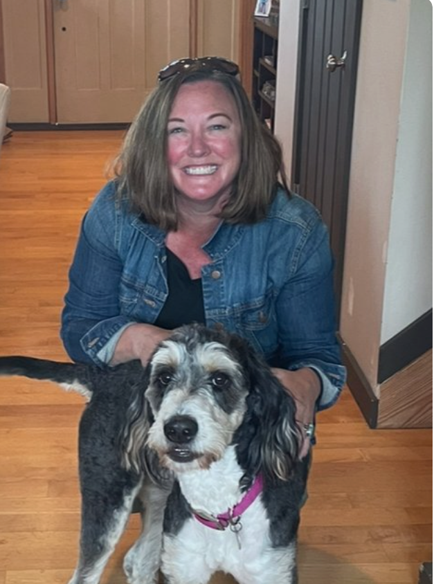 Smiling woman crouches behind a black-and-white dog in a hallway
