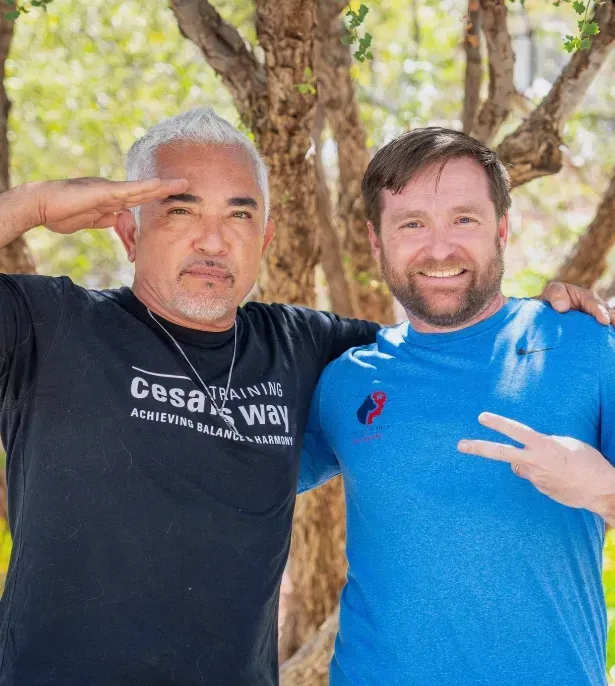 Two men posing outdoors, one saluting and the other flashing a peace sign.