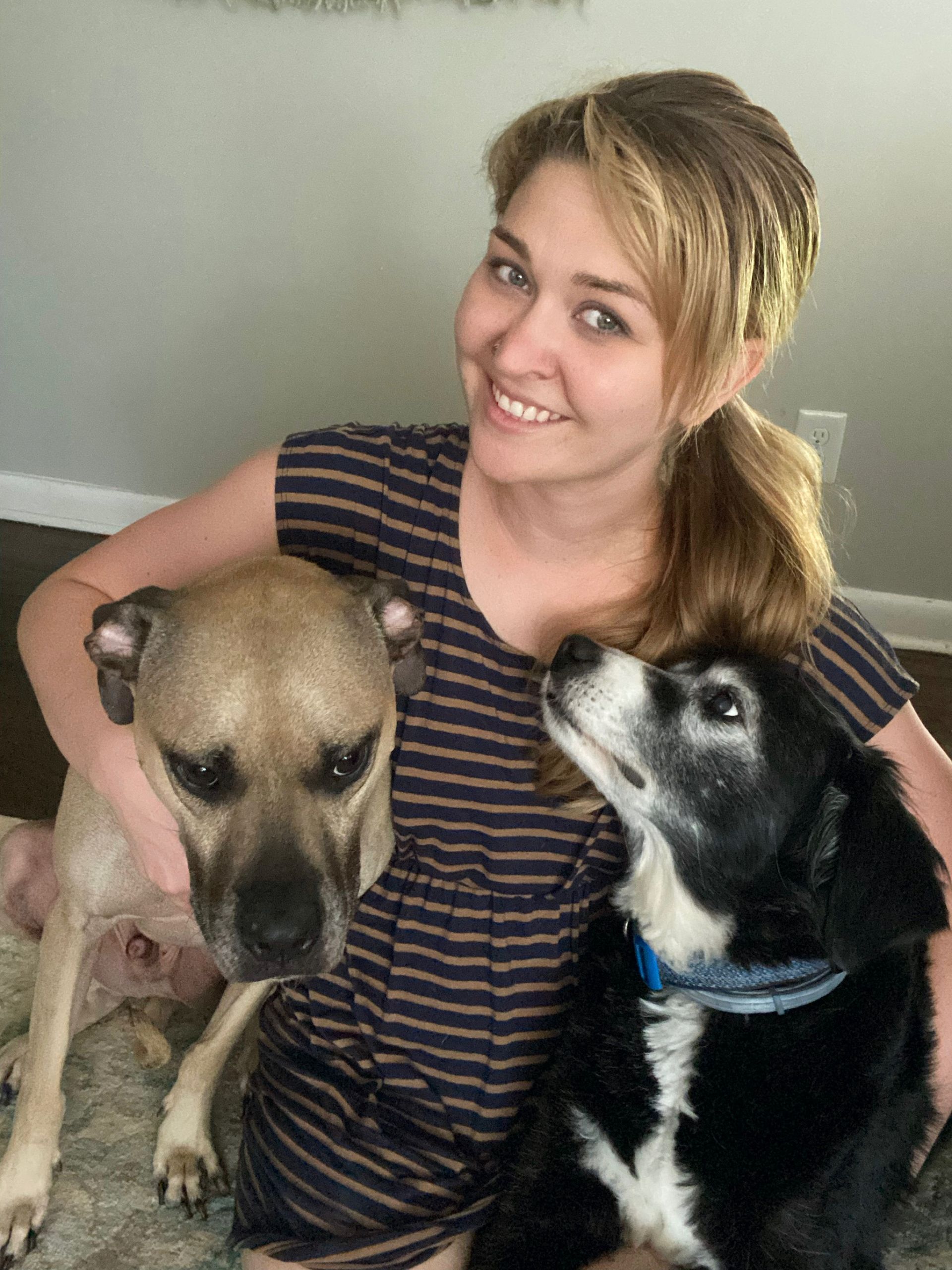 Woman sitting with two dogs, one tan and one black-and-white, indoors, smiling at the camera