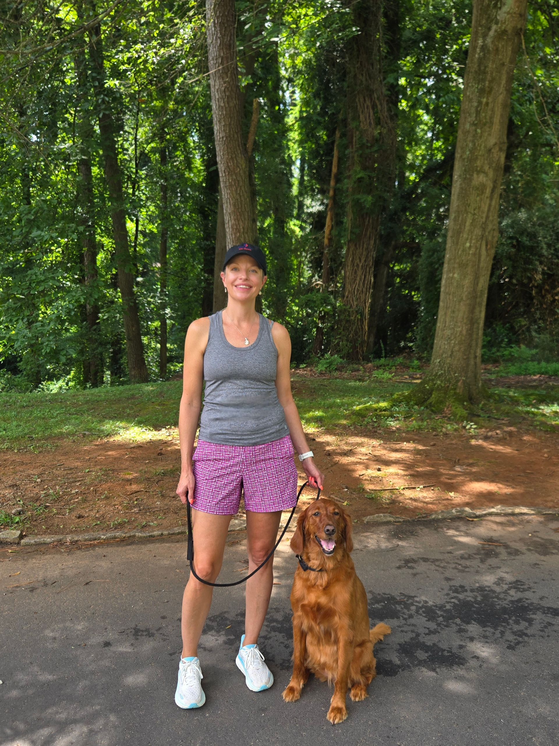 Woman standing on a wooded path with a brown dog on a leash