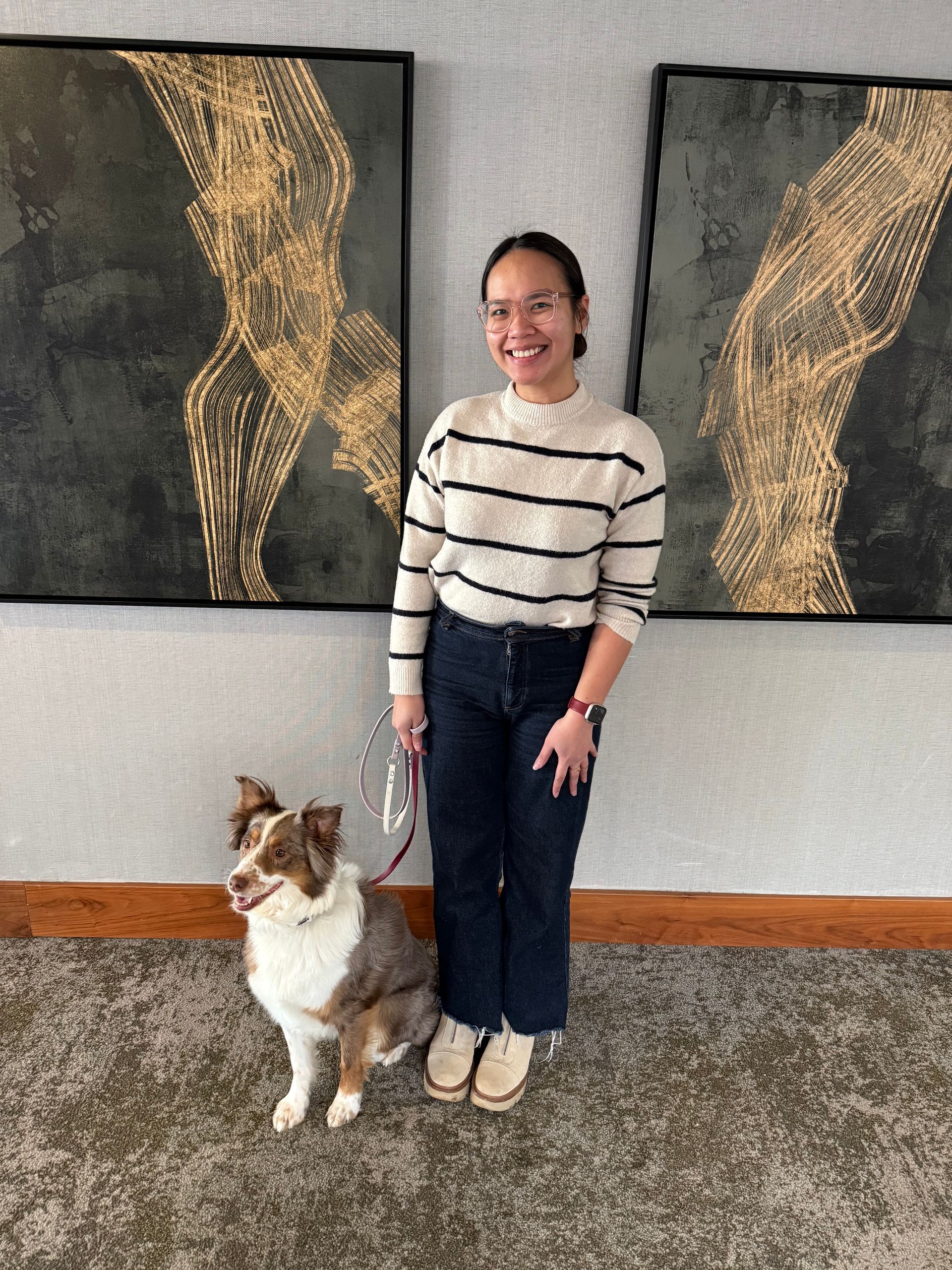 Woman standing indoors with a dog beside her in front of two abstract wall paintings.