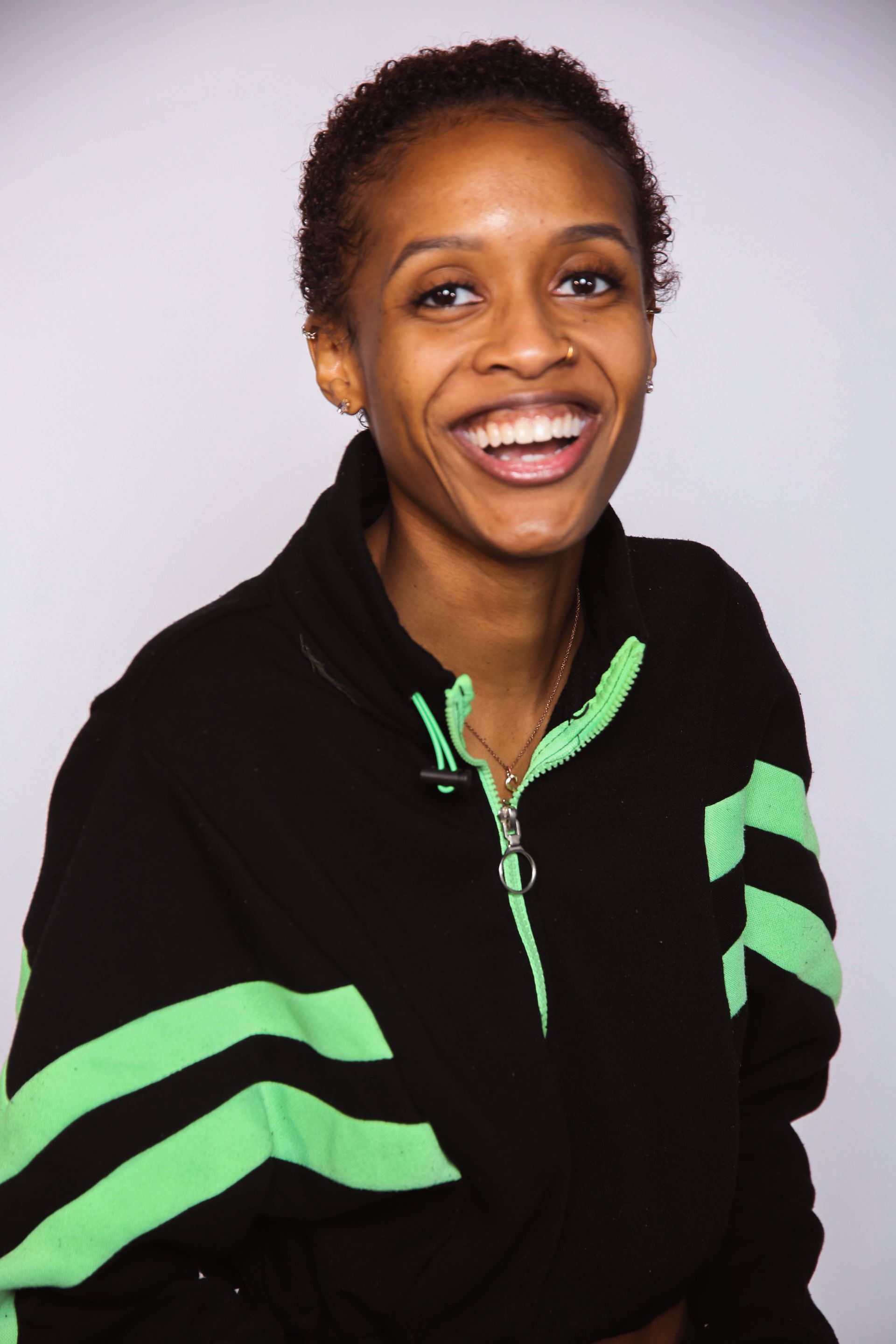 Smiling person in a black jacket with bright green stripes against a light background