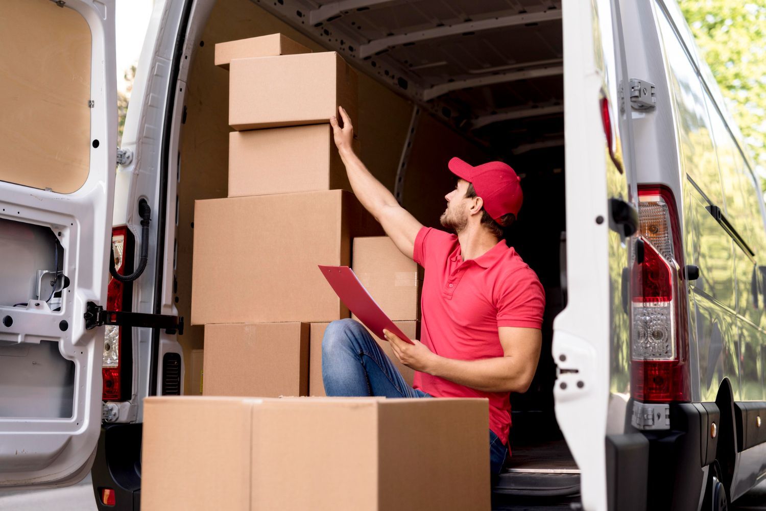Delivery person in red shirt and cap checks boxes in a van.