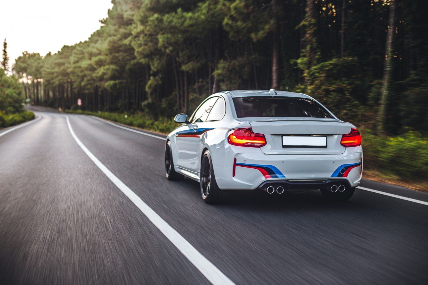 White BMW sports car driving on a tree-lined road.